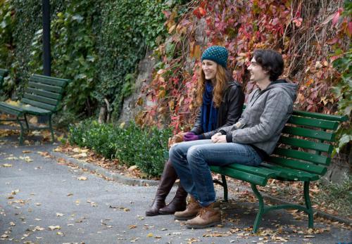 Sur le tournage du film Myrtille, un plan moyen de Marie-Eve Musy et Baptiste Gilliéron qui rient sur un banc dans un parc en automne.